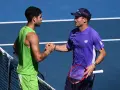 Dos tenistas, uno con camiseta verde y otro con morada, se dan la mano en la red. Tommy Paul, con gorra, sonríe tras el partido.