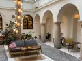 Przytulna kawiarnia patio z łukami i kolumnami. Goście siedzą przy stolikach, a obok stoi wygodna sofa. Widać rośliny i dekoracyjne lampki. Menu czeka na odkrycie.