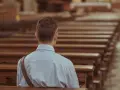 Mężczyzna siedzi w pustej ławce kościelnej, pogrążony w zadumie. To chwila wyciszenia i duchowości.