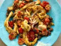 Calamari gratinati al forno su piatto blu, con pomodorini e olive.