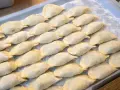 Ułożone na tacy surowe pierogi, posypane mąką.