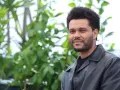 The Weeknd trägt eine schwarze Lederjacke vor einem grünen, unscharfen Hintergrund.