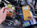 Testing for a parasitic draw with a multimeter connected to the car battery. A reading of 01.0 mV indicates a small current drain.