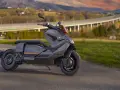 Szary skuter elektryczny BMW CE 04 na tle malowniczego krajobrazu z mostem i wzgórzami.