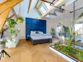 Mansarde da sogno con letto blu, piante sospese e un giardino interno in vetro. Travi a vista e lucernari creano un'atmosfera unica.