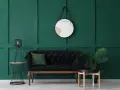 Un elegante divano nero con cuscino verde, un tavolino con lampada e una pianta, e uno specchio dietro il divano su una parete verde scuro.