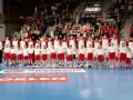Kadra piłka ręczna Polski z dziećmi na boisku, w tle kibice z flagami.