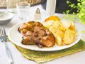 Contramuslos de pollo jugosos y dorados con patatas asadas en un plato blanco.