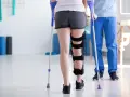 Rehabilitacja stopy po złamaniu: pacjentka z ortezą i kulami ćwiczy pod okiem fizjoterapeuty.