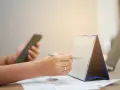 Ręce planują zadania na kalendarzu, trzymając telefon. Zapewnia to ciągłość pracy i organizację dnia.