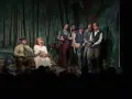 Aktorzy na scenie, w tle las. Rozmowy przy wycinaniu lasu, gdy grupa ludzi w strojach z epoki dyskutuje.