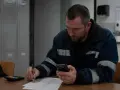 Pracownik w roboczym ubraniu sprawdza telefon, notując coś na papierze. Może to być jego dodatek nocny 2025.