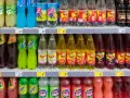 Półki sklepowe z różnymi napojami gazowanymi w plastikowych butelkach.