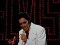 Elvis Presley singt "If I Can Dream" in einem weißen Anzug vor einer roten Lichterwand.