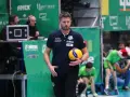 Trener Michał Piwowarczyk z piłką siatkową w dłoni, gotowy do akcji na boisku.