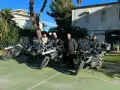 Czterech motocyklistów w pełnym rynsztunku gotowych na **prom na Sycylię**. Motocykle BMW GS zaparkowane na zielonym placu, w tle budynek i palmy.