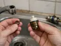 Mains pour remplacer joint robinet ancien. Une bague d'étanchéité noire est tenue dans une main, à côté d'une cartouche de robinet démontée.