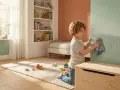 Niño limpiando huellas de manos en una pared con pintura pizarra. Juguetes y cama infantil en la habitación.