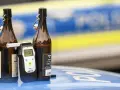 Zwei Bierflaschen und ein Alkoholtester auf einem Polizeiauto. Der Tester zeigt 0.00, aber die Gefahr einer 1 1 Promille Strafe bleibt.