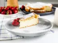 Pyszna Karpatka a ptysie z kremem, posypana cukrem pudrem, z truskawkami na talerzu.