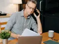 Mann am Telefon, der Dokumente prüft. Frustriert, weil die Kfz-Versicherung nicht zahlt.