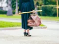 Elegancka kobieta w czarnej sukni i czarnych szpilkach, niosąca brązową torbę i żółty kij. Uosobienie francuskiej mody.