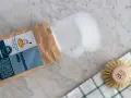 Percarbonato sódico, ideal para ropa color, se derrama de su bolsa junto a un cepillo.