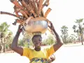 Kobieta w Burkina Faso niesie na głowie misę z drewnem, z dzieckiem na plecach.