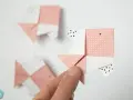 Hand hält Origami-Fisch. Mehrere rosa und weiße Papierfische, die gefaltet wurden, sind im Hintergrund zu sehen.