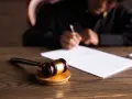 Młotek sędziowski na drewnianym stole. W tle osoba pisze dokument. Czy uprawomocnienie wyroku przychodzi pocztą?