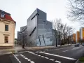 Nowoczesny budynek Muzeum Żydowskiego w Berlinie, obok zabytkowej kamienicy, z charakterystyczną, poszarpaną fasadą.