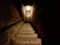 Escaleras de hormigón que bajan hacia una puerta en un sótano oscuro con una luz tenue.