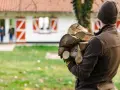 Chcesz wiedzieć, jak zostać leśniczym? Ten mężczyzna z drewnem na podpałkę, w tle dom z czerwonymi okiennicami i dzieci, pokazuje, że praca w lesie to też praktyczne zadania.