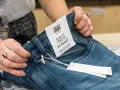 Dłonie trzymają niebieskie jeansy z metką "SLIM FIT STRETCH 34 WAIST". Idealny rozmiar jeansów dla Ciebie.