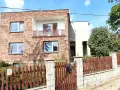 Nowoczesna metamorfoza domu z lat 80. z ceglaną fasadą, balkonem i drewnianym płotem.