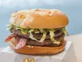 Duży burger z dwoma kotletami, bekonem i sałatą na białym opakowaniu.