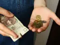 Dłoń trzyma banknot 20 zł i garść monet. Symbolizuje to spłatę długu po wyroku sądowym, gdzie każda złotówka ma znaczenie.