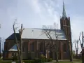 Sanktuarium w Swarzewie, ceglany kościół z wysoką wieżą, otoczony drzewami o nagich gałęziach.