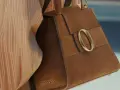Borsa in camoscio marrone con fibbia dorata. La texture morbida evidenzia la differenza tra camoscio e pelle scamosciata.