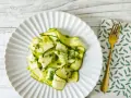 Delicato carpaccio di zucchine condito con erbe fresche, servito su un piatto bianco con forchetta dorata.