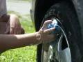 A person's arm and hand, covered in suds, scrub a car tire with a blue sponge. It seems they are testing if you can use dish soap to wash your car.