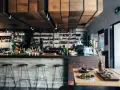 Ambiente restaurante moderno con barra, taburetes y aperitivos en mesa.