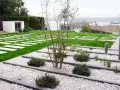 Vialetti giardino moderni con lastre quadrate su prato verde e aiuole di ghiaia bianca con piante succulente e arbusti.