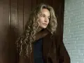 Kobieta z kręconymi, beżowymi włosami, którym pasuje ten odcień. Elegancka stylizacja z brązową marynarką.