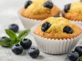 Pyszne muffiny z borówkami, ozdobione świeżymi owocami i listkiem mięty. Idealne na deser.