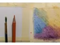 Un pinceau et un crayon aquarelle orange sont prêts pour l'utilisation. Une zone de papier présente des dégradés de couleurs vives.