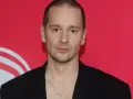 Krzysztof Zalewski w czarnym garniturze, z naszyjnikiem, na tle czerwonym z białym logo.