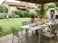 Famiglia che pranza all'aperto, con bambini che giocano a calcio. Perfette idee zona relax giardino per godersi la vita.