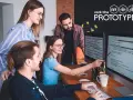 Ein Team von vier Personen arbeitet im **mob programming** an einem Projekt. Sie blicken auf zwei Bildschirme mit Code.
