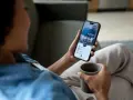 Kobieta z kawą sprawdza na telefonie, jak sprawdzić zadłużenie komornicze, analizując finanse domowe.